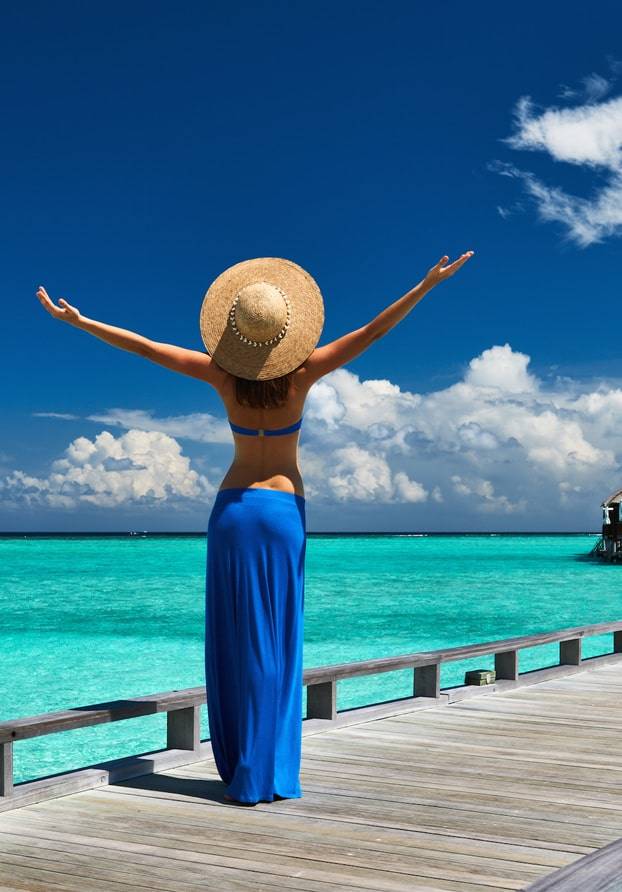 Woman standing on pier with arms raised over ocean