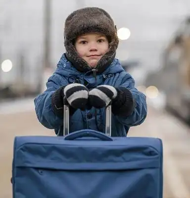 Child wearing winter clothes sitting on a suitcase