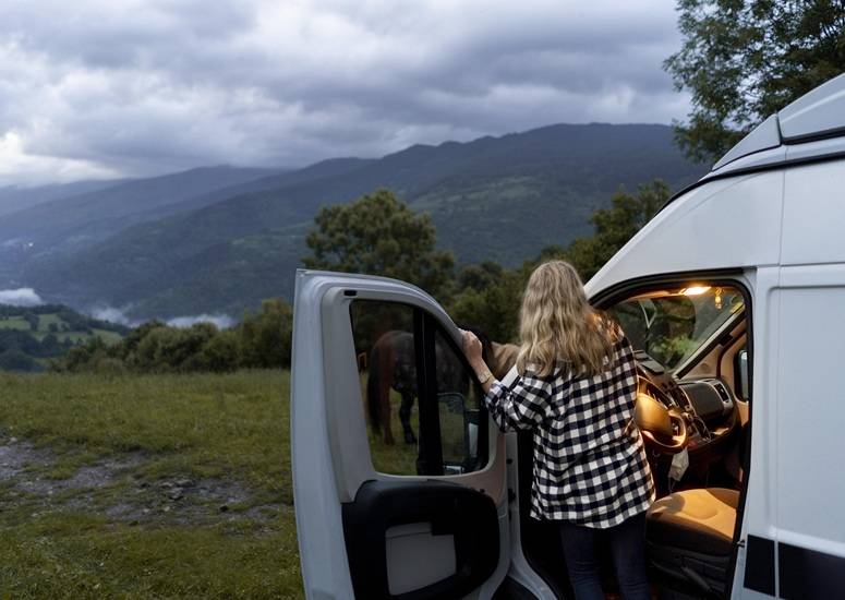Woman standing by a van in a scenic mountain landscape